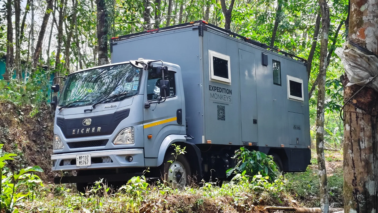 Bhanumati, the Strofes-built expedition camper, parked among tall forest trees — a purpose-built habitat on a commercial truck chassis.